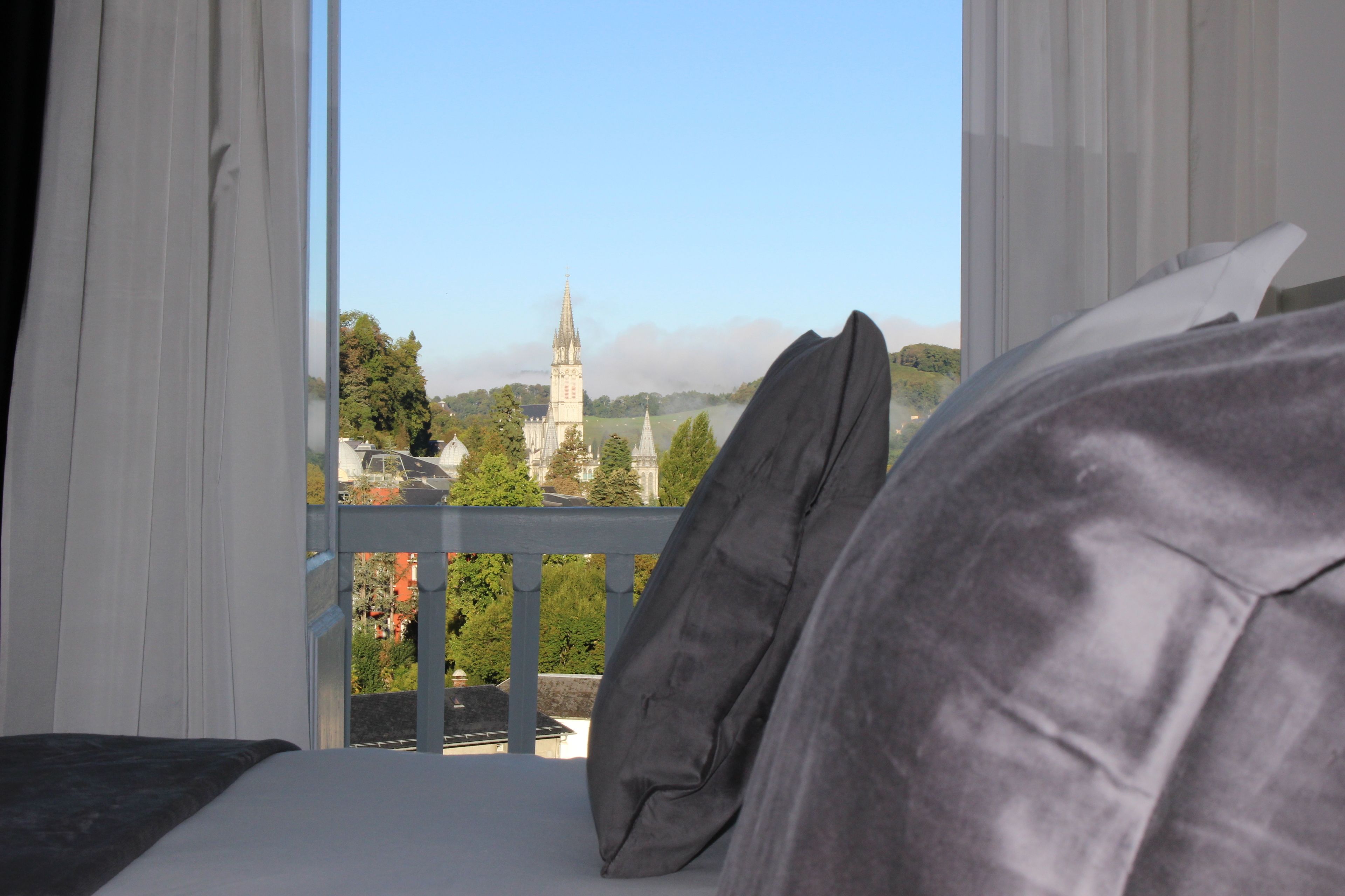 A hotel room with a balcony overlooking a cityscape, including a prominent church tower.