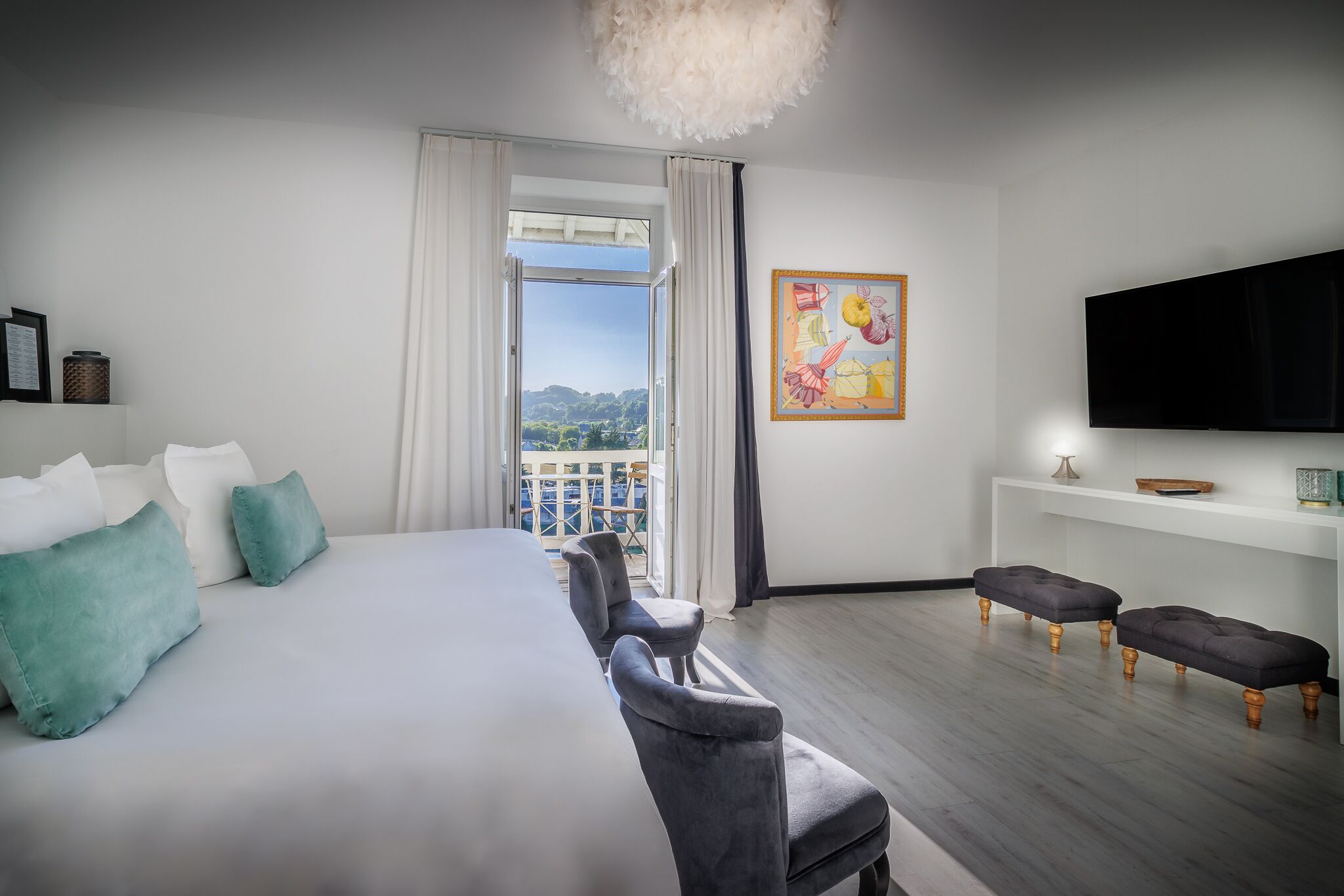 Ein modernes Hotelzimmer mit einem großen Bett, grauen Polstersesseln, einem Flachbildfernseher und einem Balkon mit Blick.
