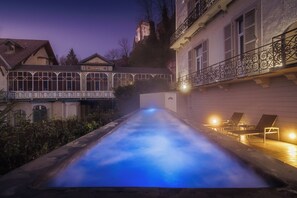 A swimming pool with a glass enclosure, lounge chairs, and a building with a balcony. - Belfry Spa by Ligne St Barth (Lourdes)