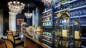 A bar area with a polished bar counter, multiple chandeliers, and shelves stocked with bottles and glasses. - Belfry Spa by Ligne St Barth (Lourdes)