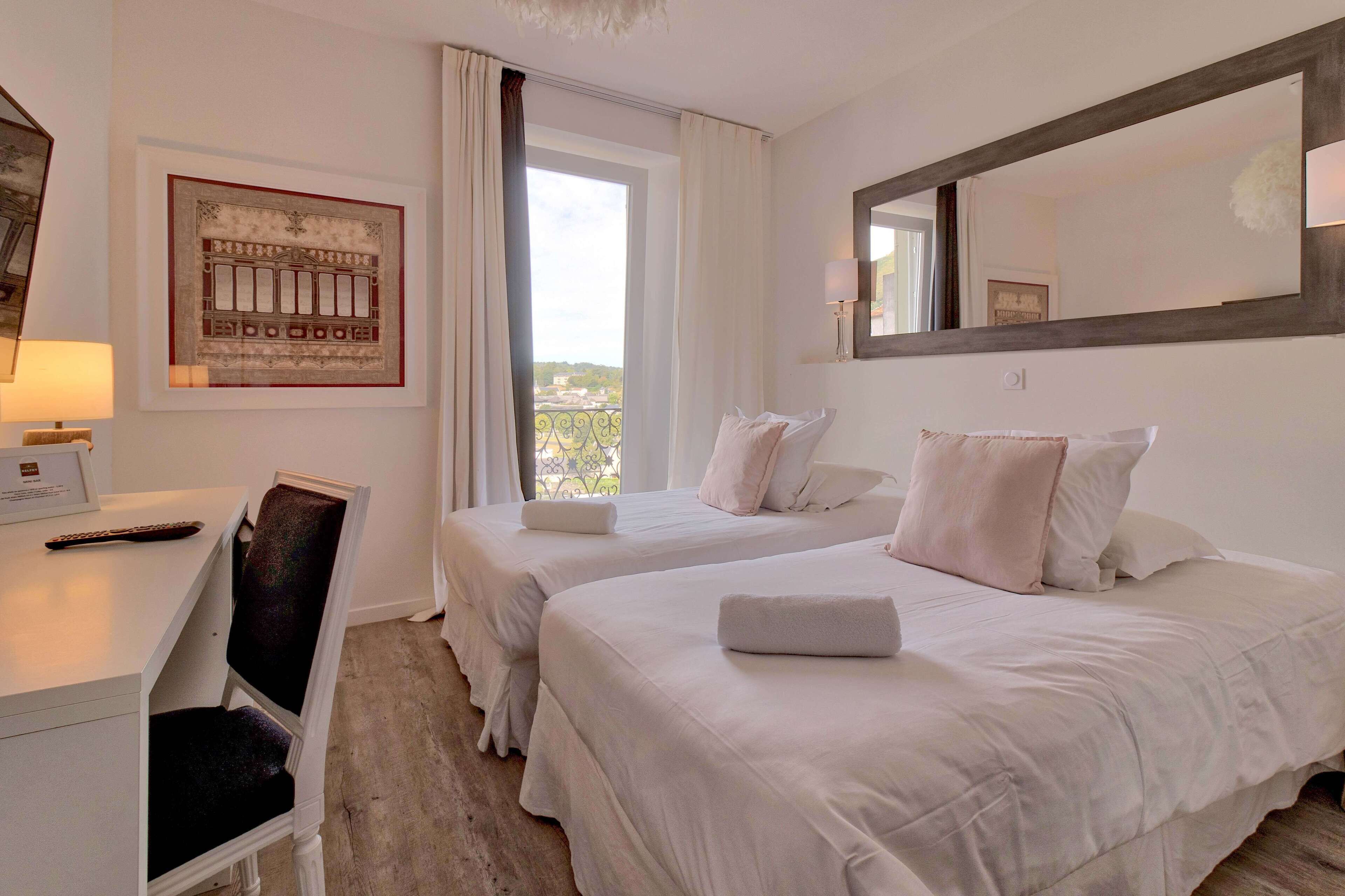 A hotel room with two beds, a desk, a chair, and a large window with curtains.