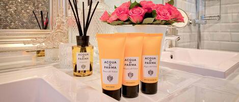 A bathroom with a white sink, a mirror, and three bottles of Acqua di Parma body cream.