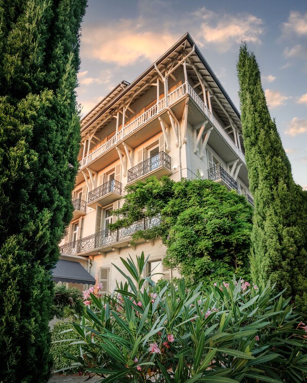 A multi-story building with balconies, surrounded by lush greenery and tall trees.