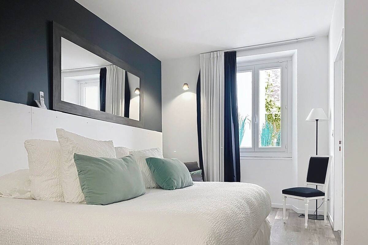 A modern bedroom with a large bed, a bedside table, a chair, and a window with curtains.