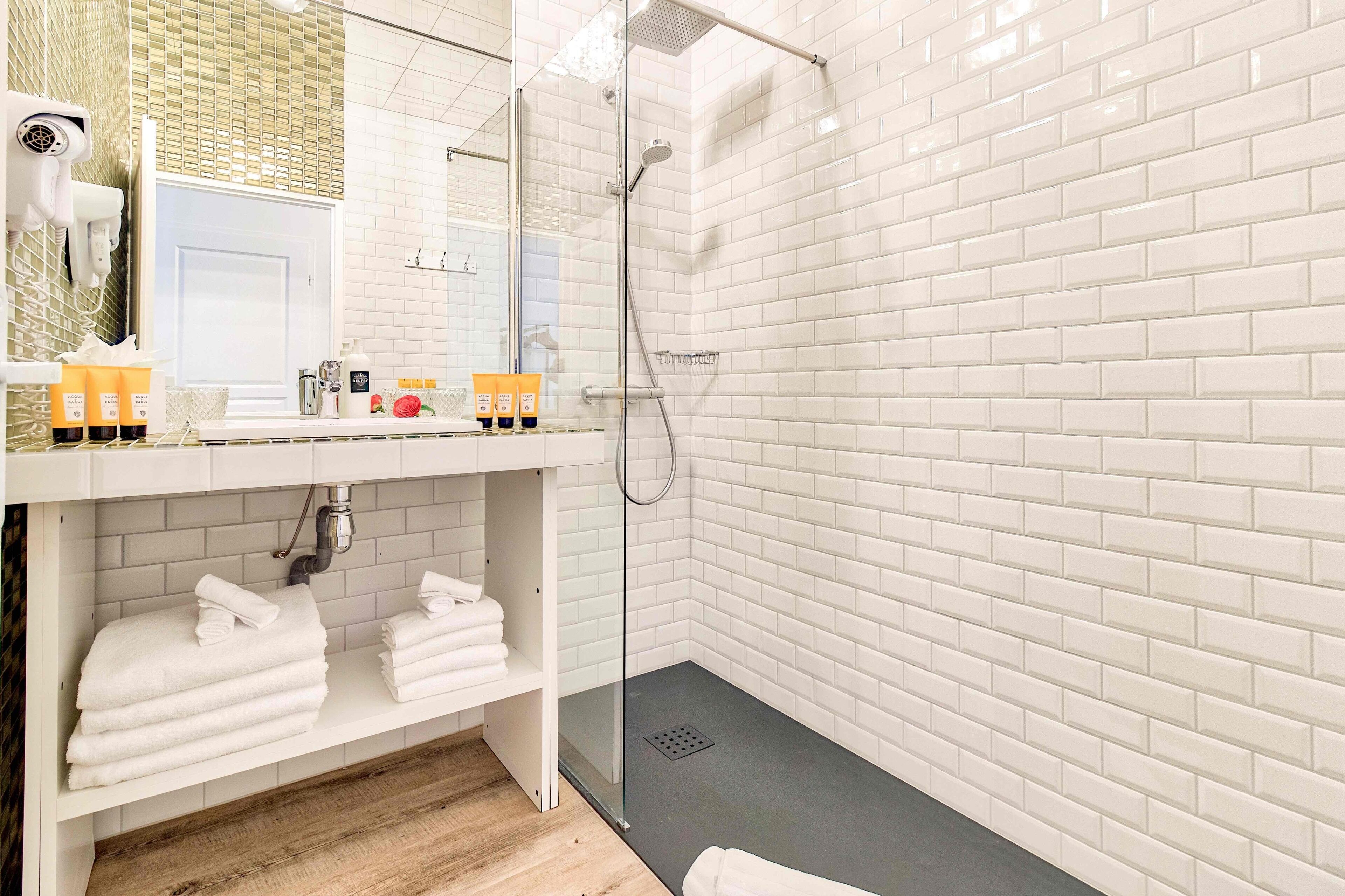 Un baño moderno con azulejos blancos tipo metro, ducha con cerramiento de vidrio y tocador con artículos de aseo.
