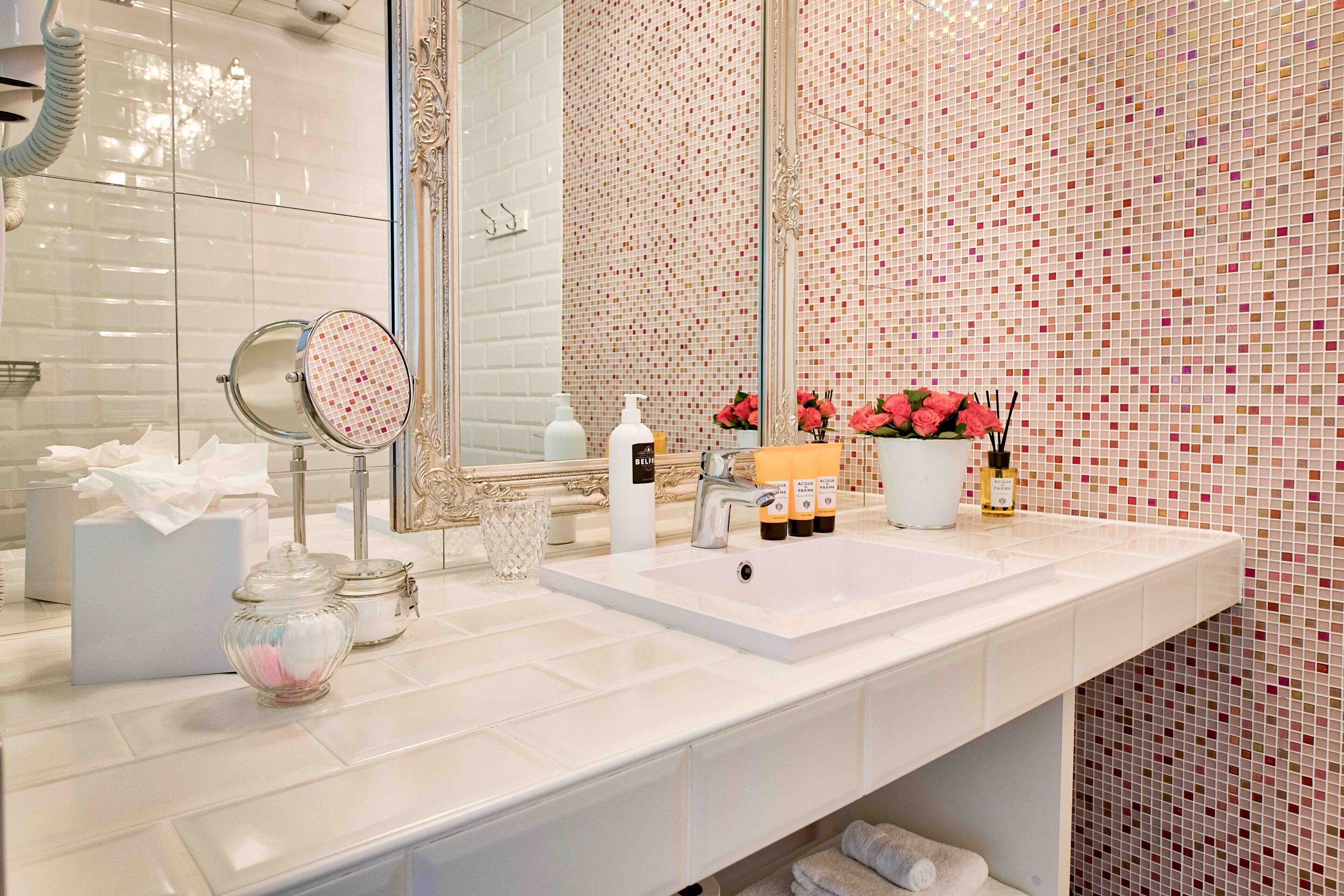A bathroom with a white sink, a mirror, a glass, and toiletries.