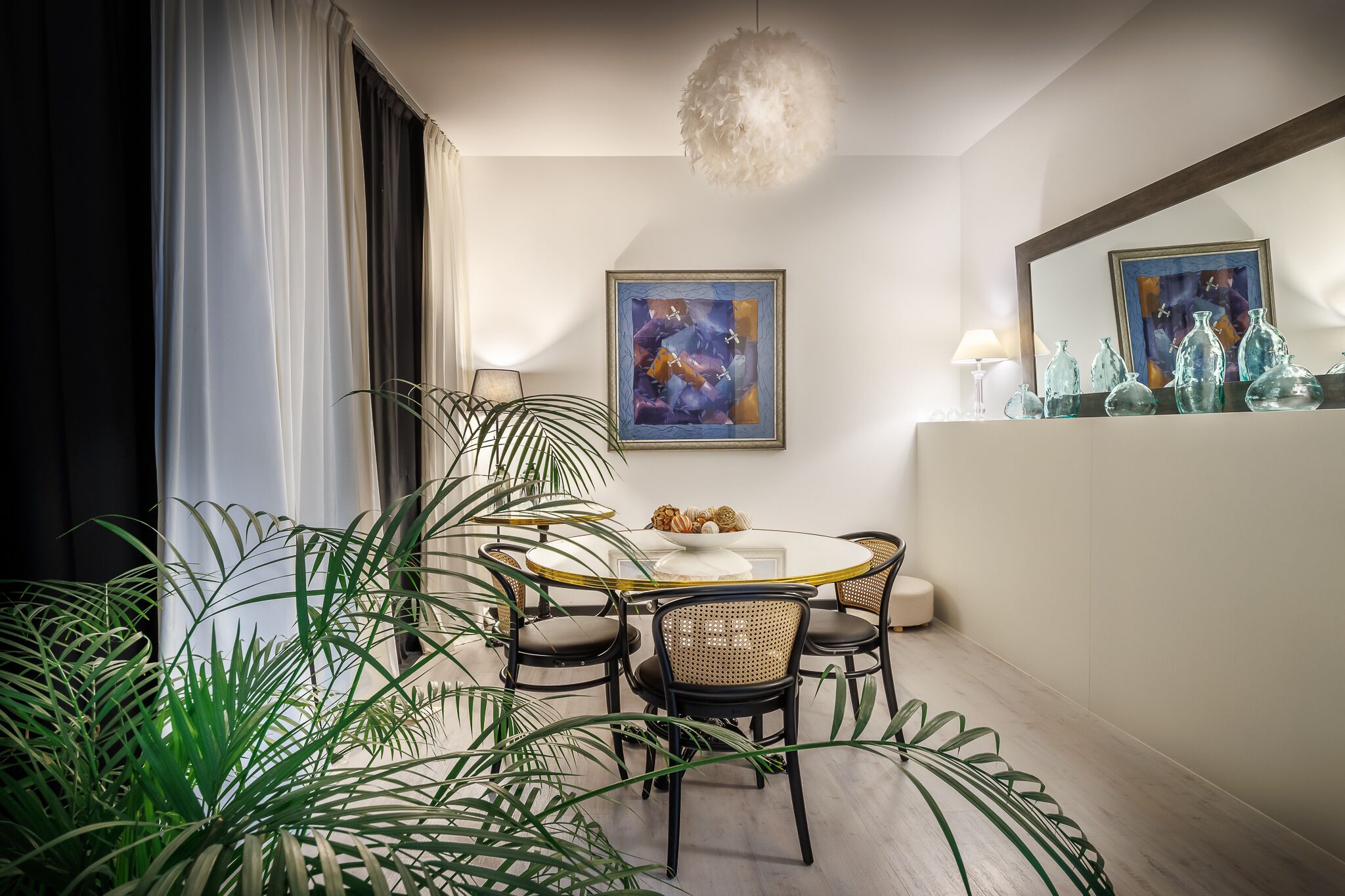 A dining area with a round table, four chairs, a white vase, and a painting on the wall.