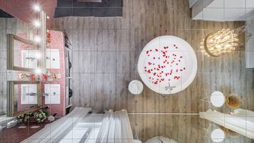 A modern bathroom with a wooden floor, a large mirror, a round sink, and a bathtub with rose petals.