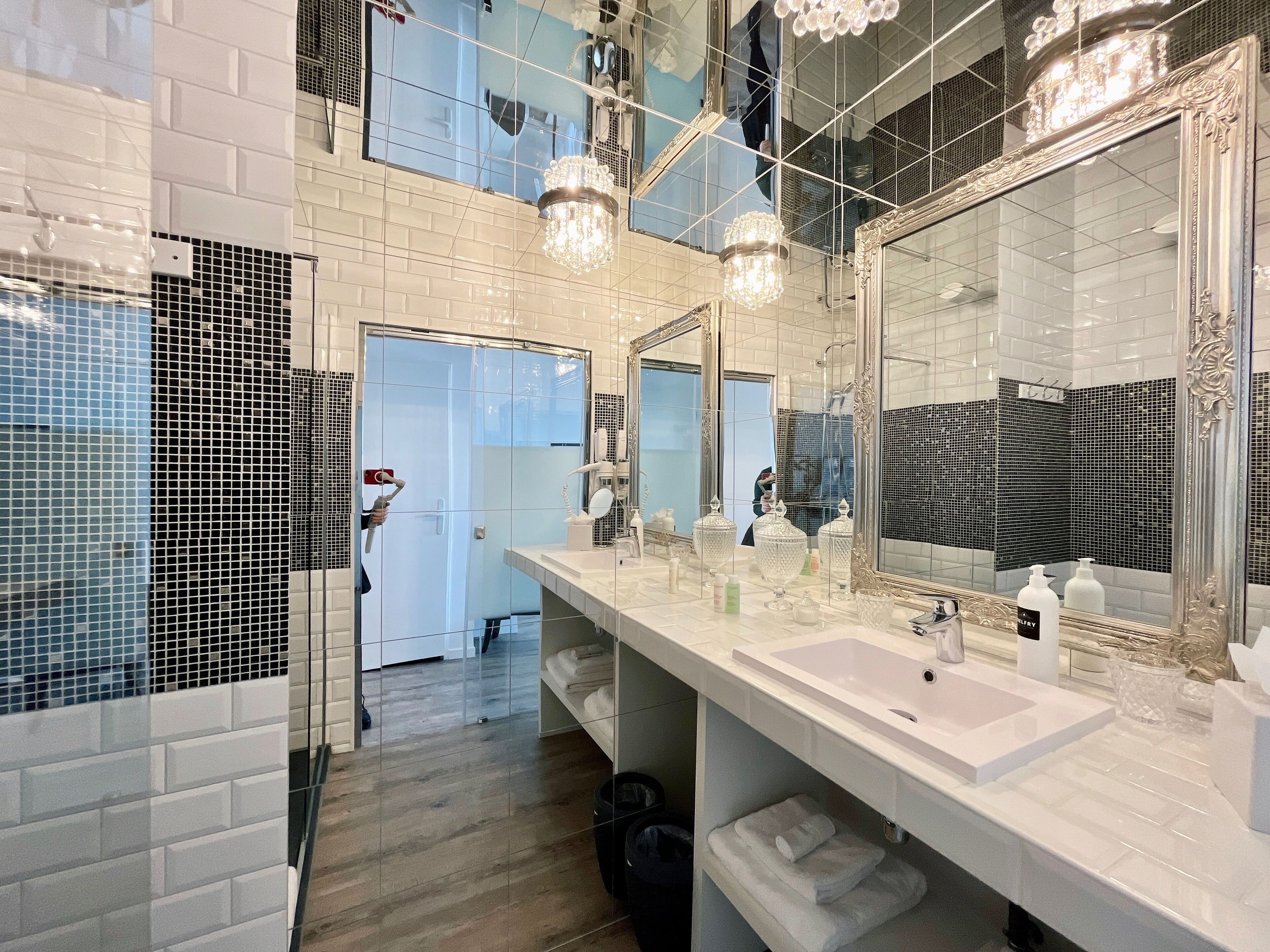 A modern bathroom with a large mirror, two sinks, and a shower area.