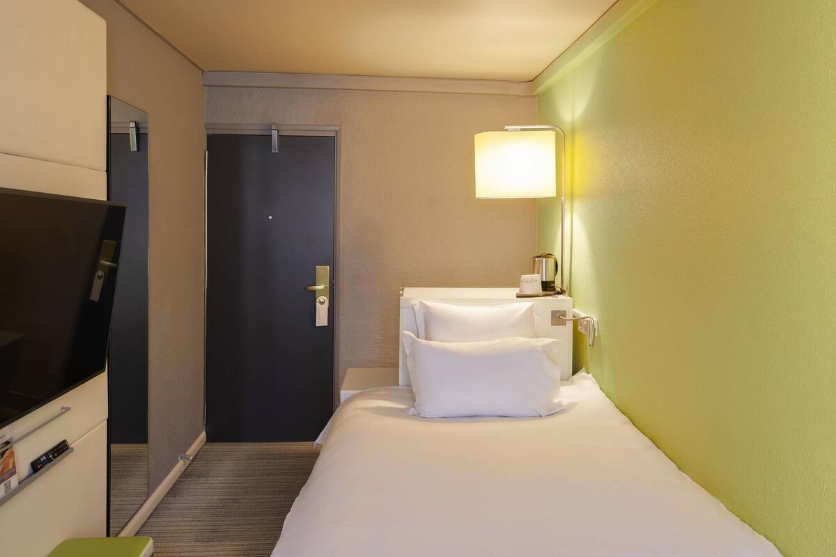 Ein Hotelzimmer mit einem Bett, einem Fernseher, einem Nachttisch und einer Lampe.