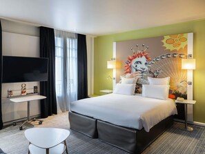 A hotel room with a bed, a desk, a chair, a TV, and a large wall mural. - Mercure Nice Centre Grimaldi (Nice)