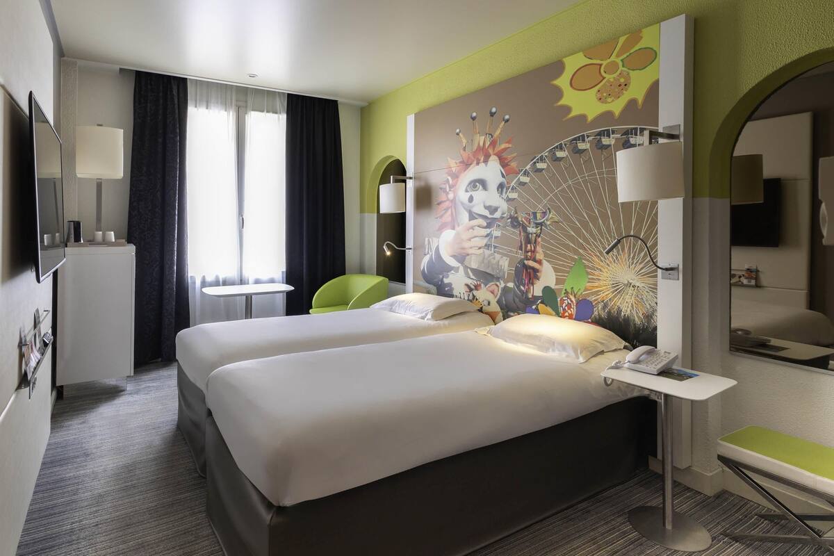 Ein Hotelzimmer mit Bett, Schreibtisch, Sessel, Fernseher und einem Fenster mit Vorhängen.