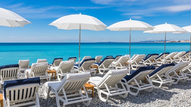 Una playa con sillas y sombrillas blancas, dispuestas en filas mirando al mar.
