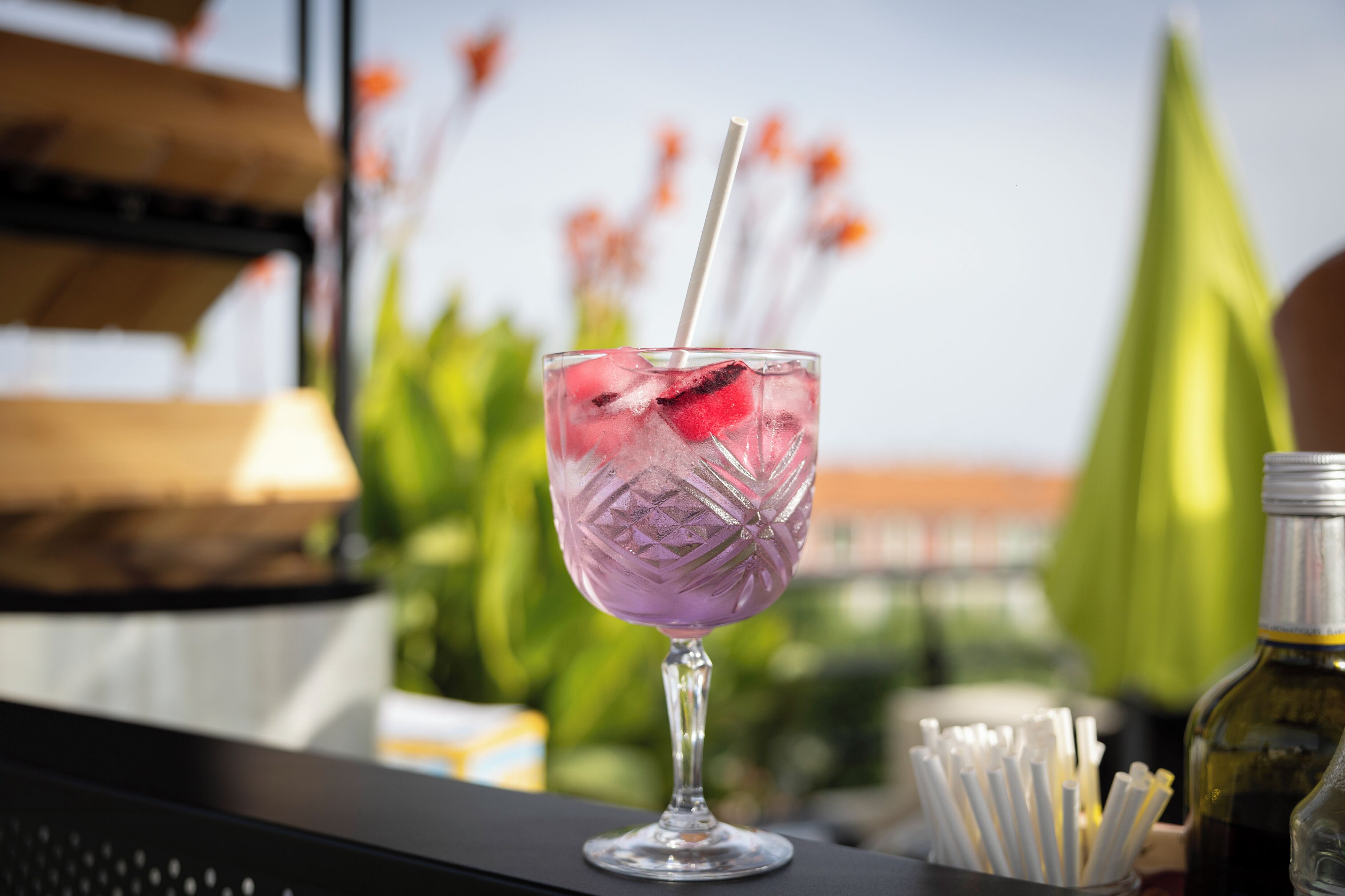 A cocktail glass with a straw, ice, and fruit on a bar counter.