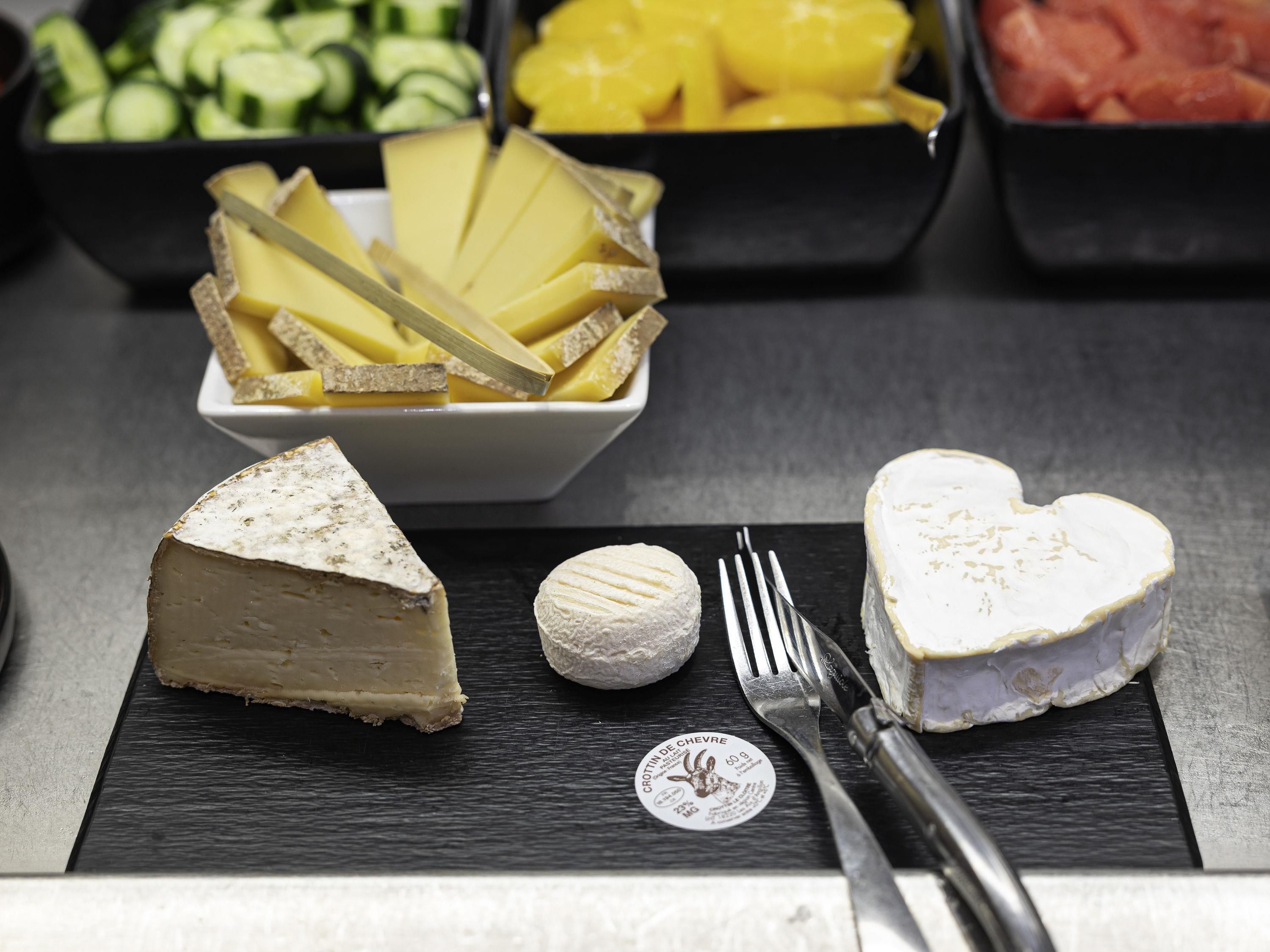 A selection of cheeses and fruits on a slate board with a fork and knife.