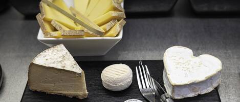A selection of cheeses and fruits on a slate board with a fork and knife.