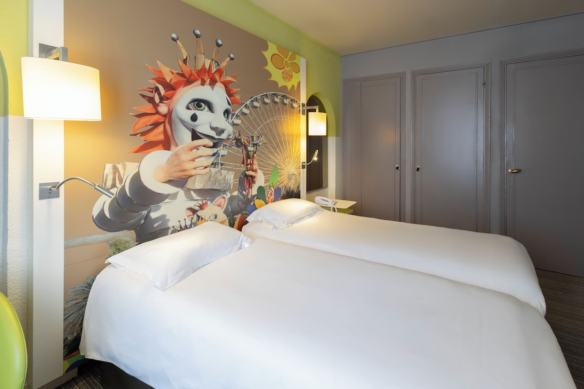 A hotel room with a large bed, a wall mural, a door, and a nightstand.