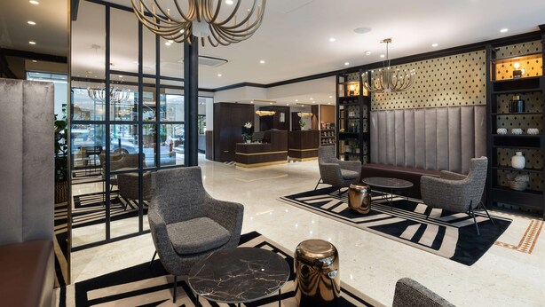 A modern lobby with seating areas, a reception desk, and a large chandelier.