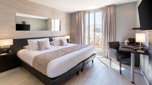 A modern hotel room with a large bed, a desk with a chair, a flat-screen TV, and a balcony with curtains.