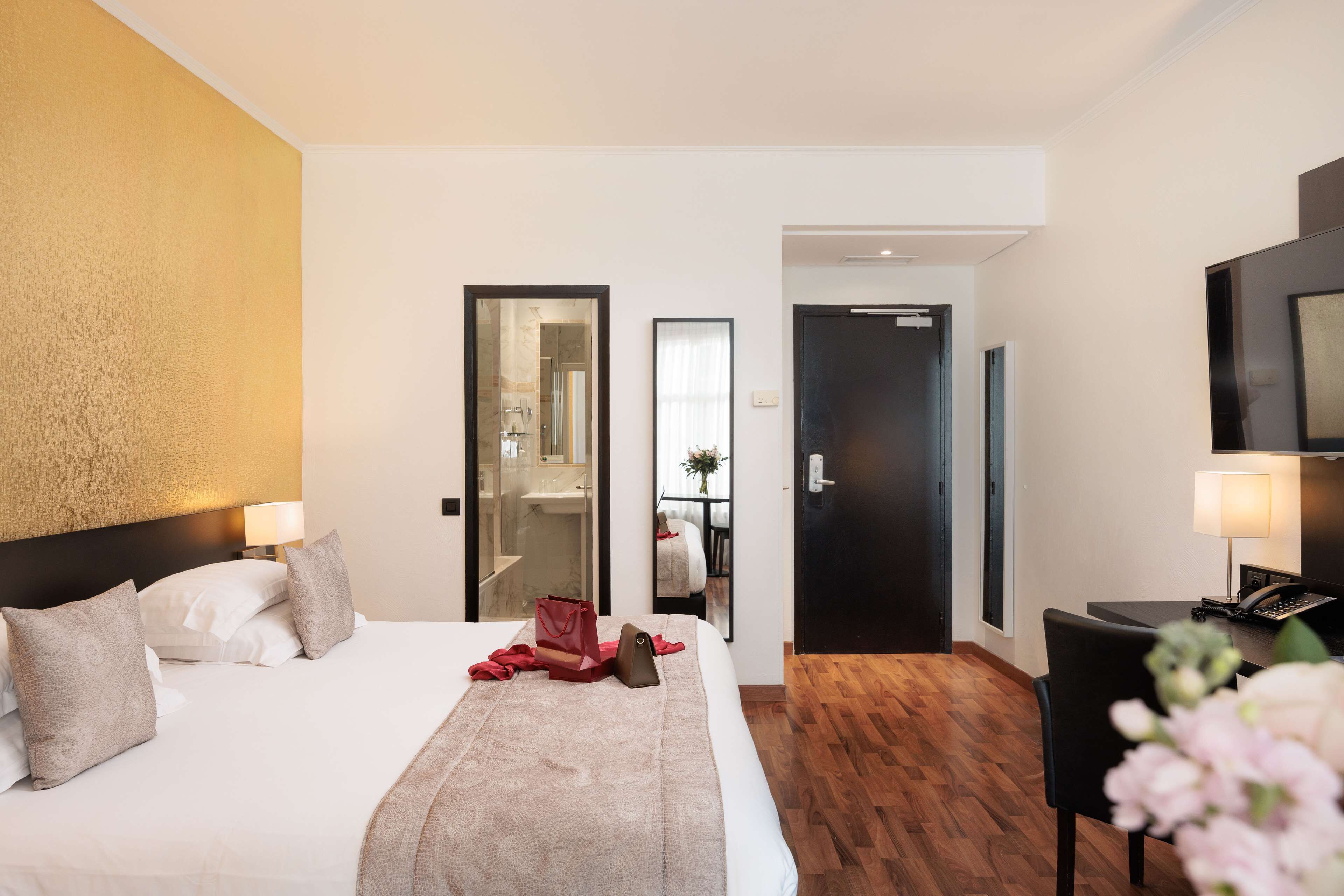A hotel room with a bed, bedside tables, a mirror, a TV, and a wooden floor.