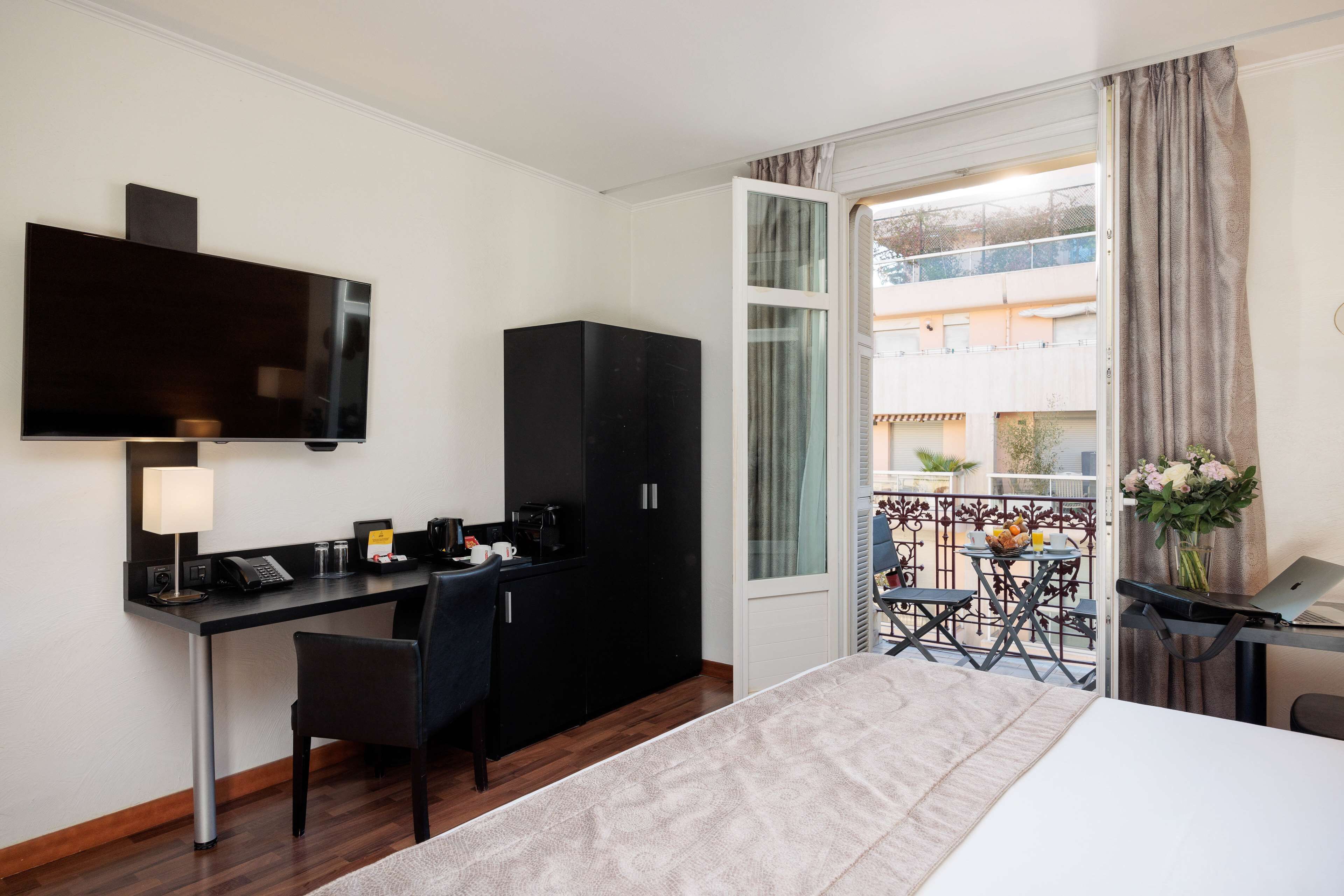 A hotel room with a bed, desk, chair, TV, and a balcony with a table and chairs.