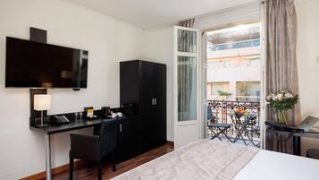 A hotel room with a bed, desk, chair, TV, and a balcony with a table and chairs.