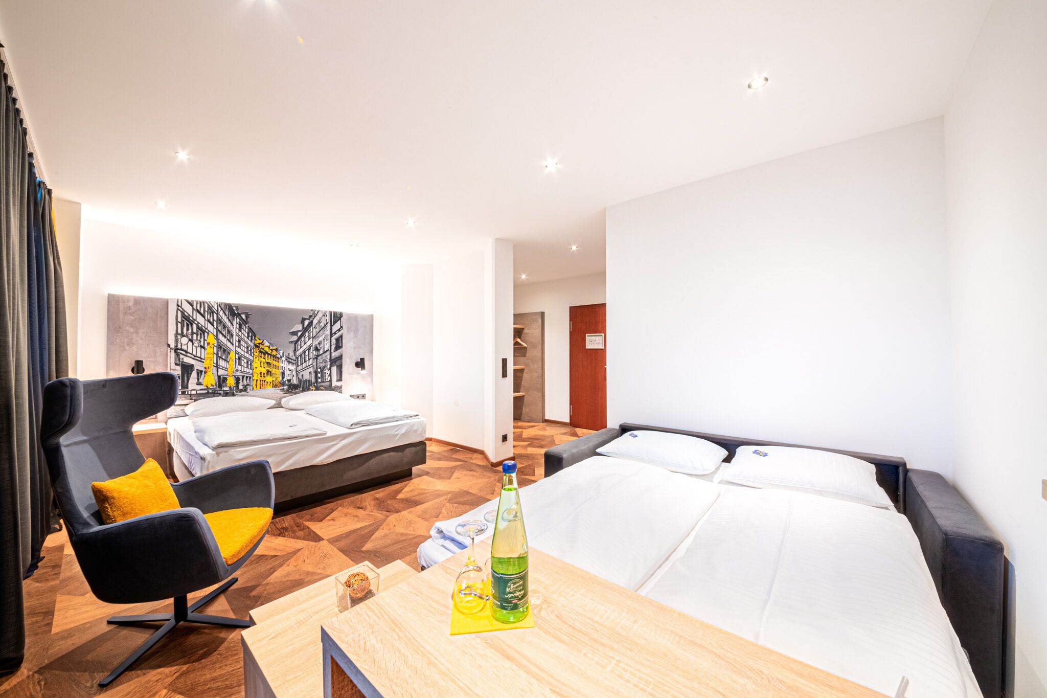 Een moderne hotelkamer met een groot bed, een slaapbank, een bureau met een fles en een stoel.