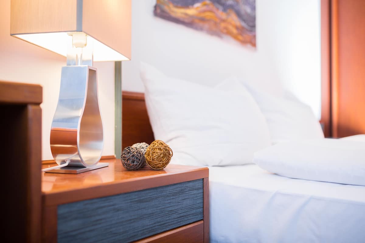 A neatly made bed with white linens, a bedside lamp, and decorative balls on the nightstand.