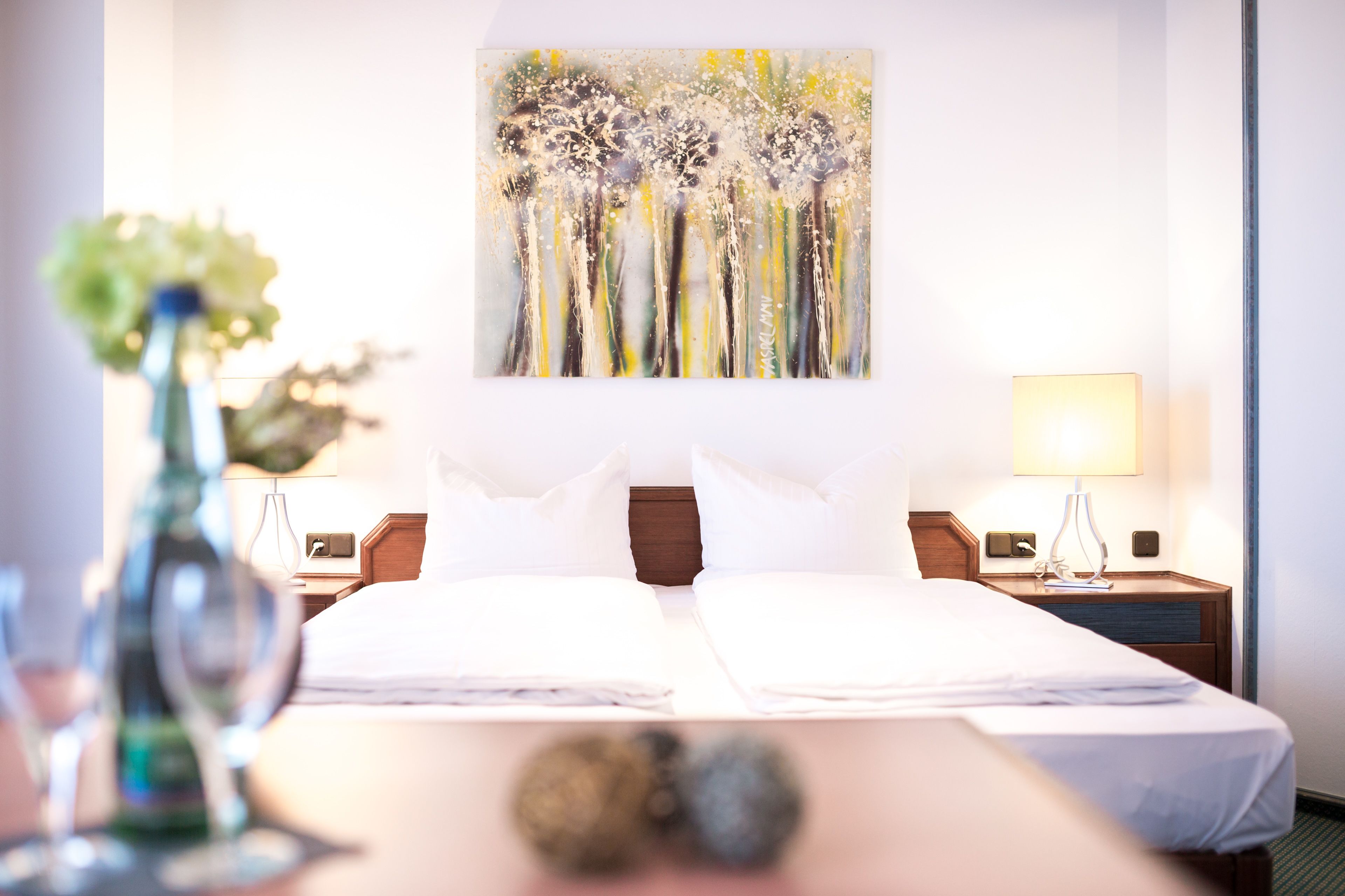 Quarto de hotel com uma cama grande, duas mesinhas de cabeceira, um criado-mudo, uma luminária e um quadro na parede.