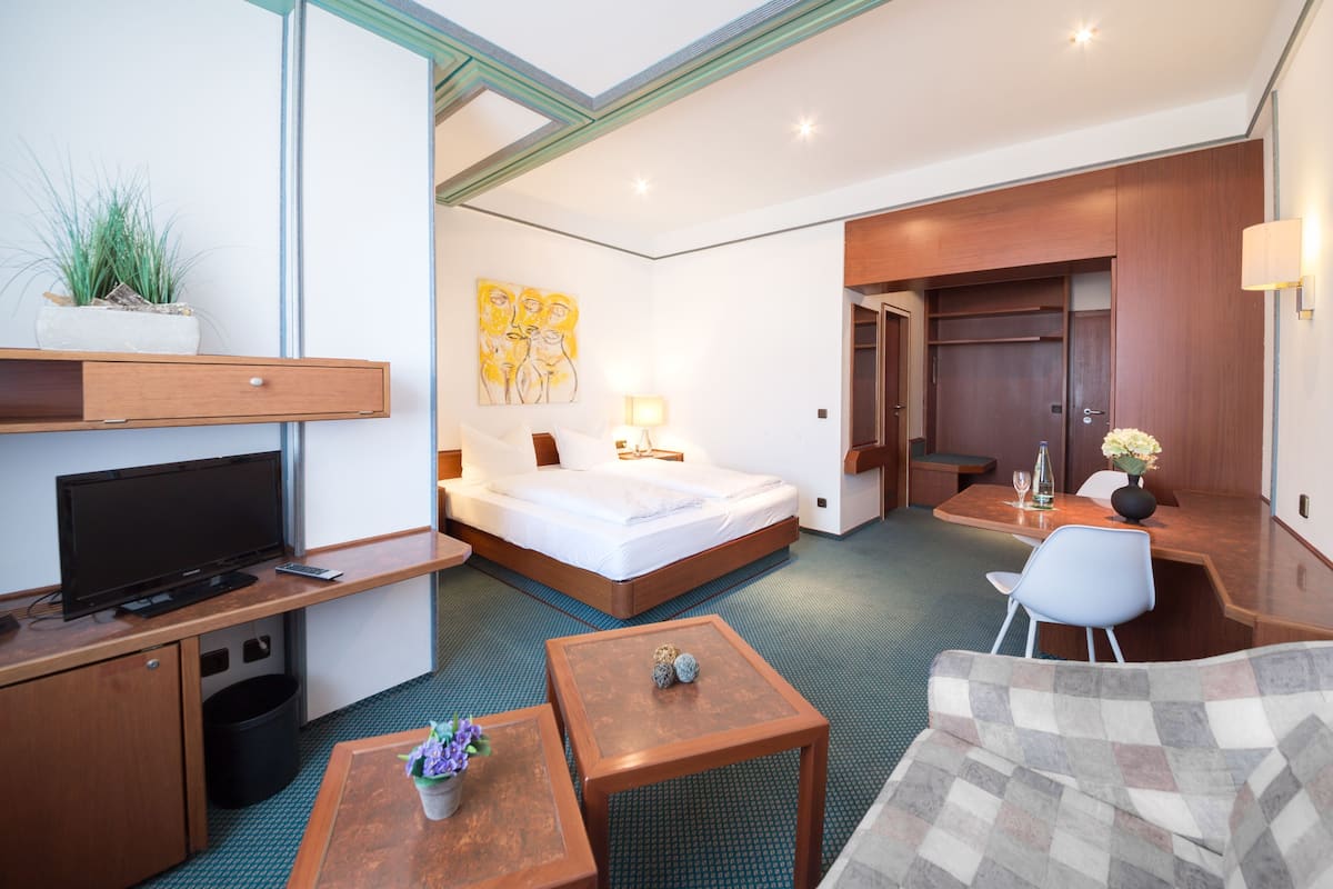 A hotel room with a bed, desk, TV, and seating area.
