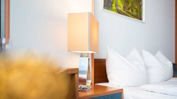 Een hotelkamer met een bed, witte kussens, een nachtkastje van hout en een moderne lamp.
