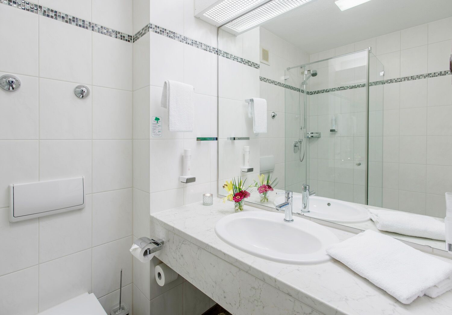 Un baño moderno con un espejo grande, dos lavamanos y una cabina de ducha de vidrio.