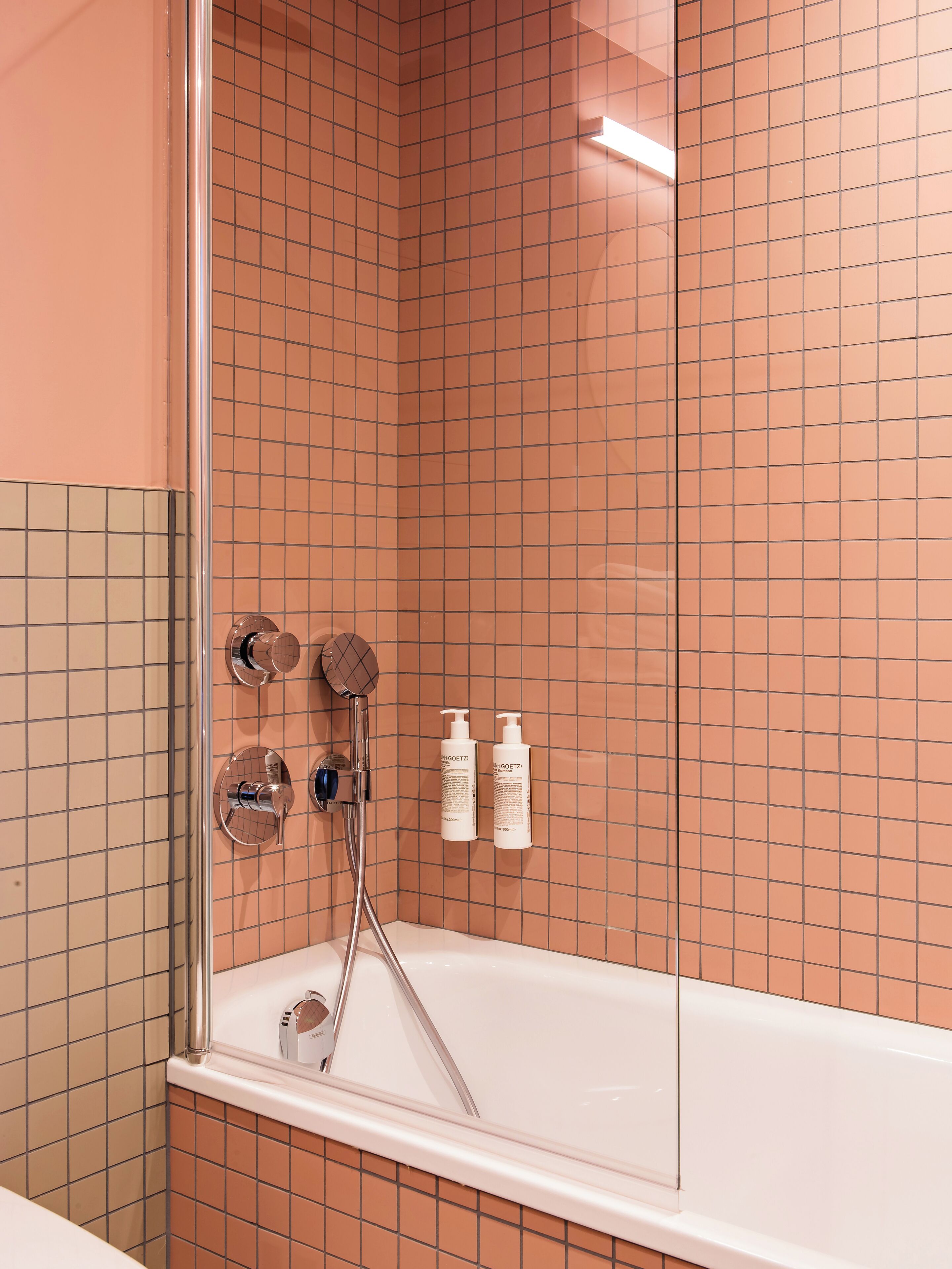 A bathroom with a glass-enclosed shower, a white bathtub, and two bottles of shampoo on the wall.
