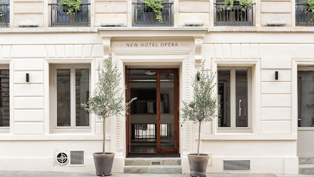 Un edifici amb un cartell que diu "NEW HOTEL OPERA" a l'entrada. Hi ha dos arbres en testos davant de l'entrada.