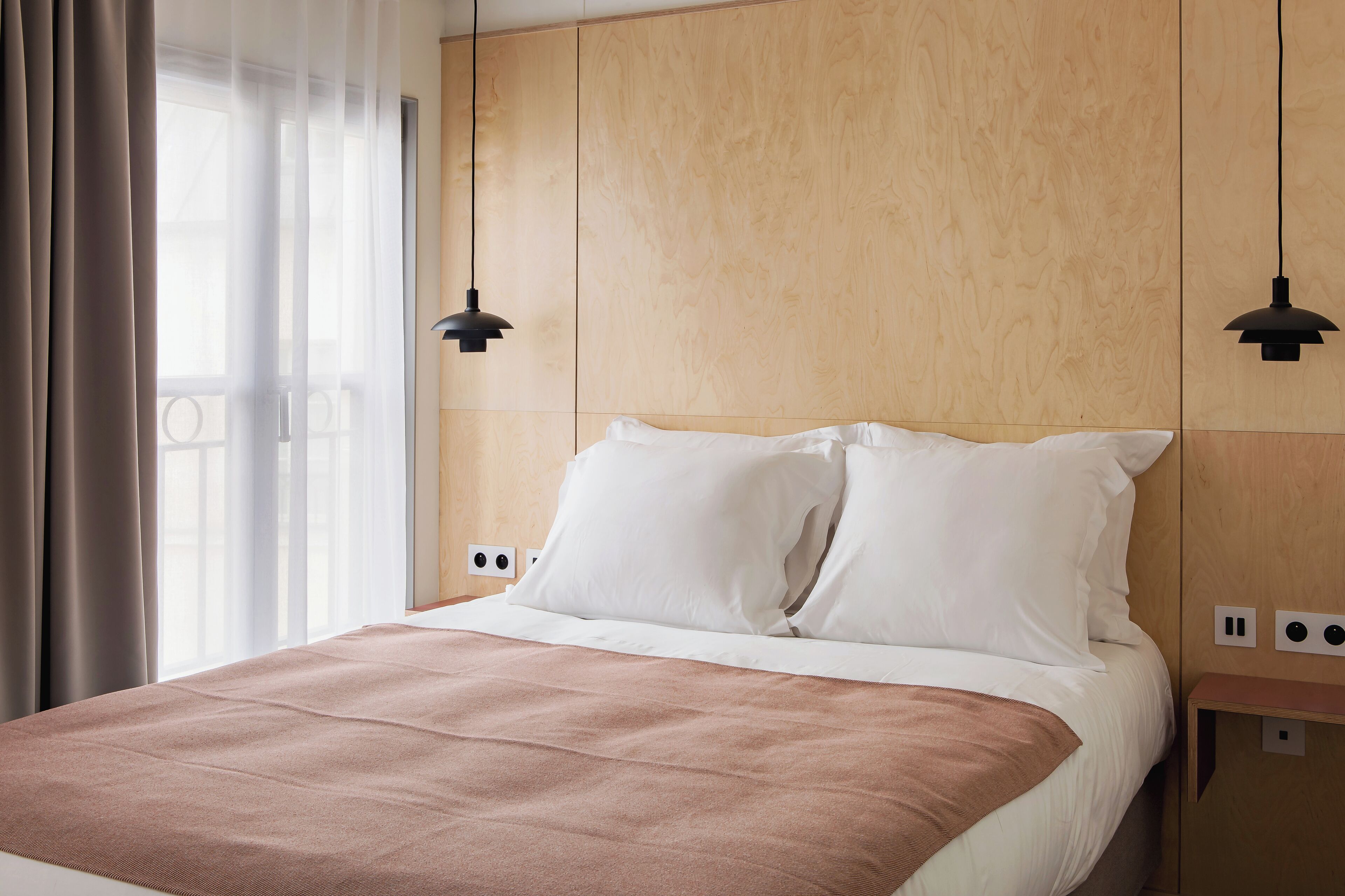 A neatly made bed with white and brown bedding, two black pendant lights, and a wooden headboard.