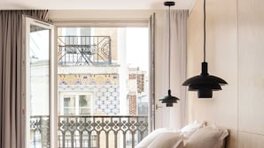 Una habitació d'hotel amb llit, vistes a la ciutat i un balcó amb barana de ferro.