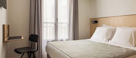 A hotel room with a bed, a chair, a window with curtains, and a wooden headboard.