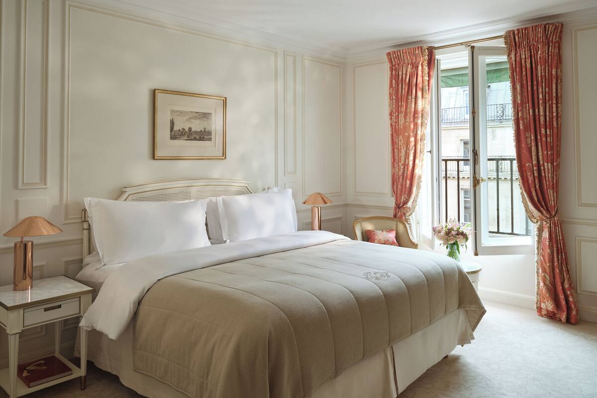 A neatly arranged bedroom with a bed, bedside tables, a lamp, and a window with curtains.