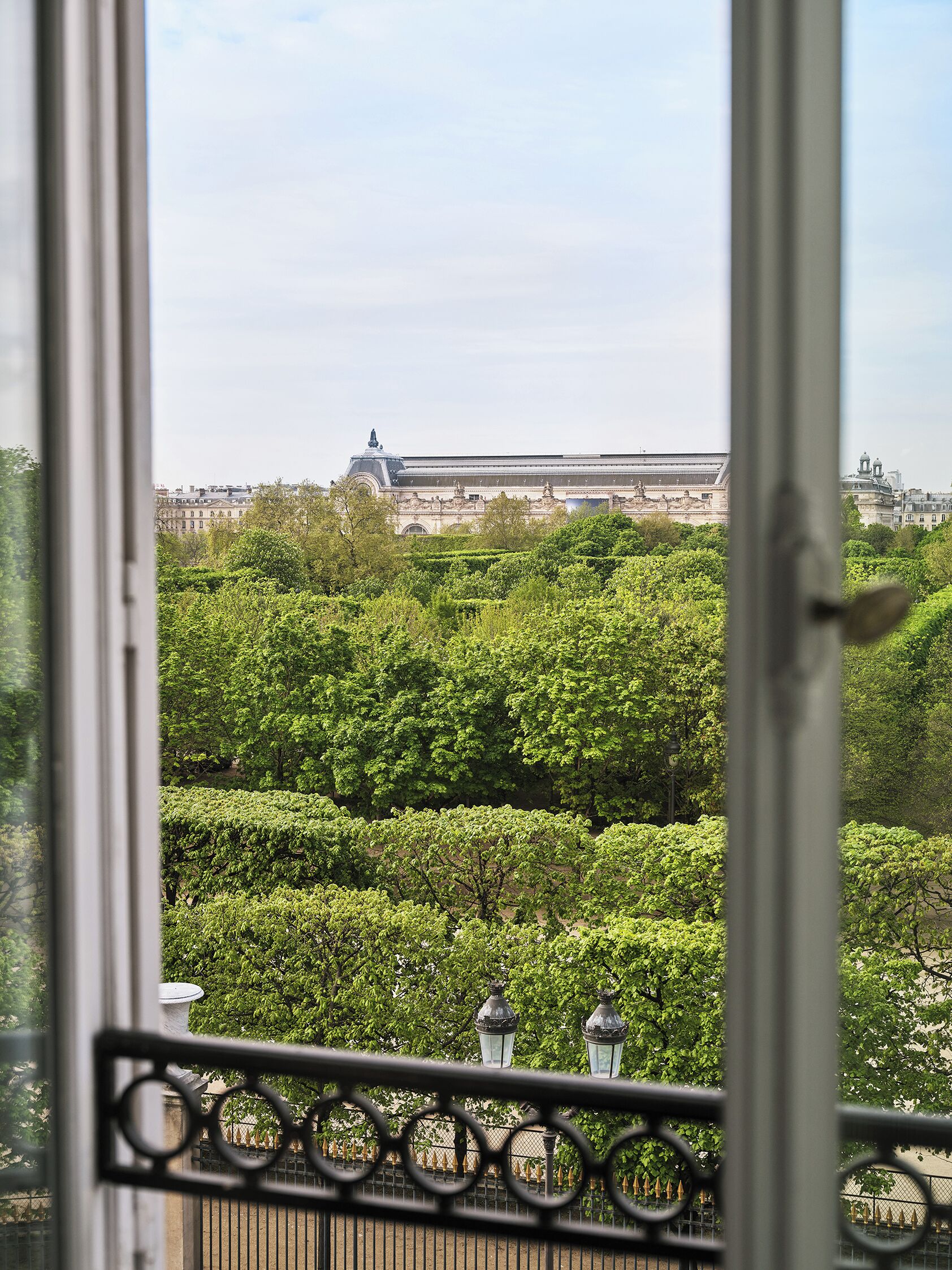 A view of a large building with classical architecture, surrounded by lush green trees and a metal fence.