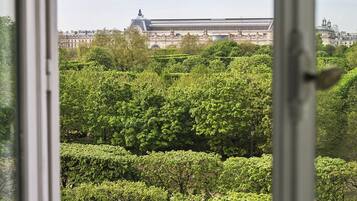 A view of a large building with classical architecture, surrounded by lush green trees and a metal fence.