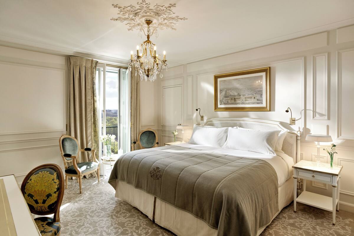 A spacious bedroom with a large bed, a chandelier, a framed picture, and a view of the outdoors.