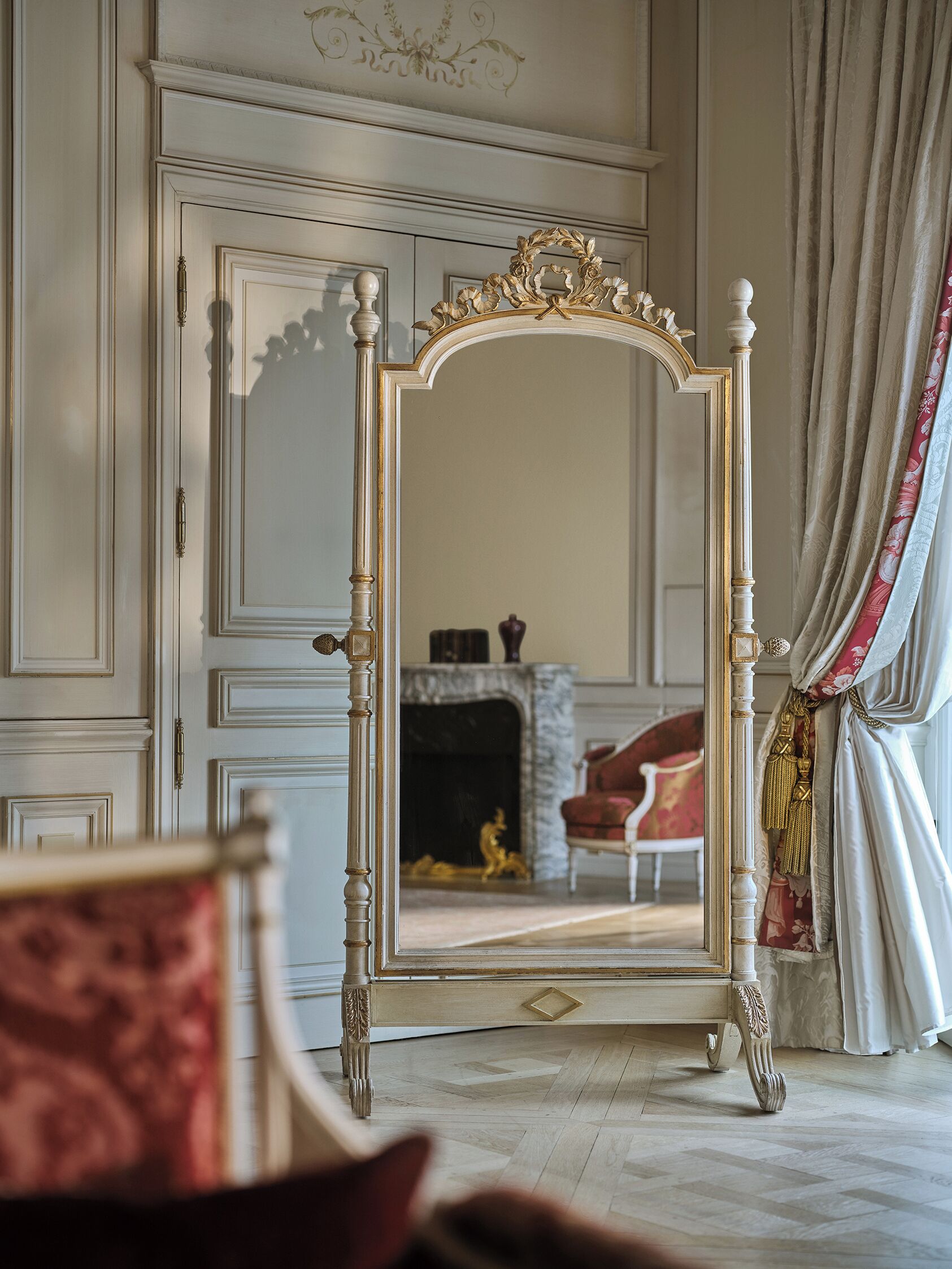 A room with a large ornate mirror, a fireplace, and a red armchair.