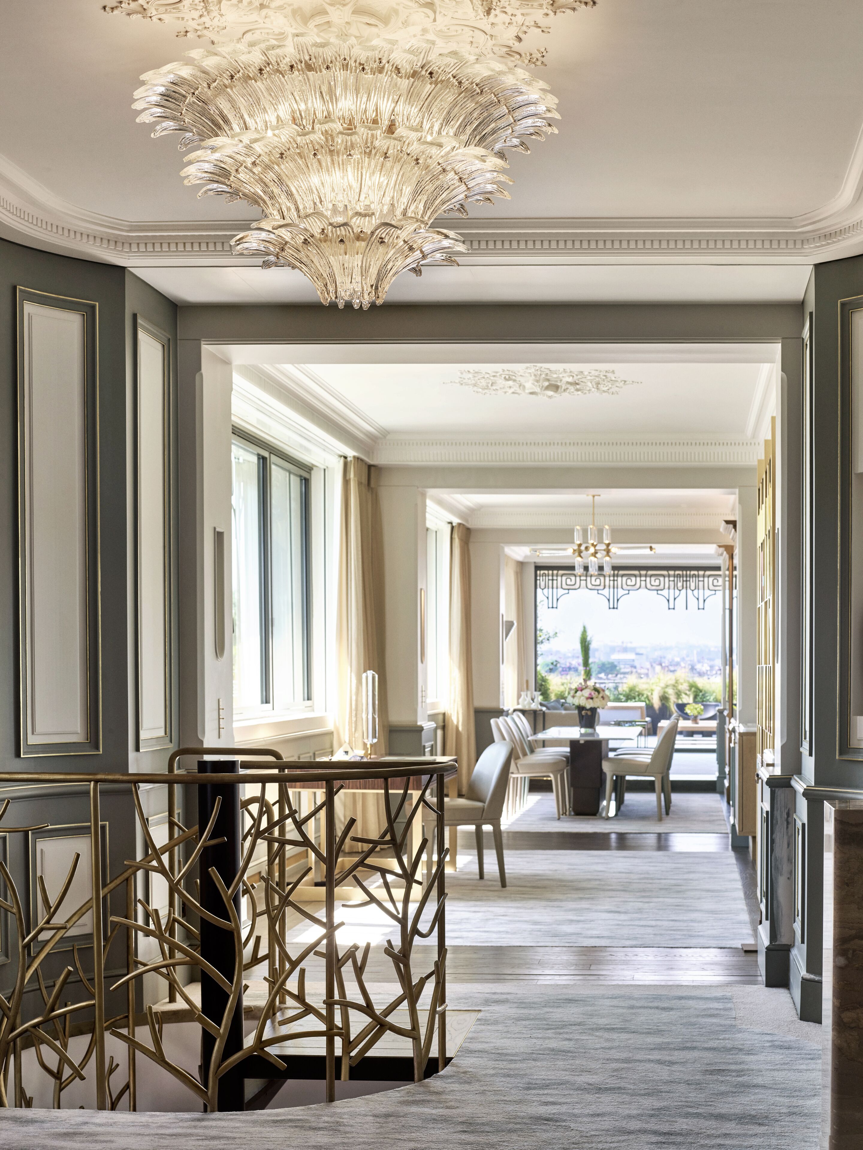 A grand hallway with a chandelier, a dining area with chairs and a table, and large windows offering a view.
