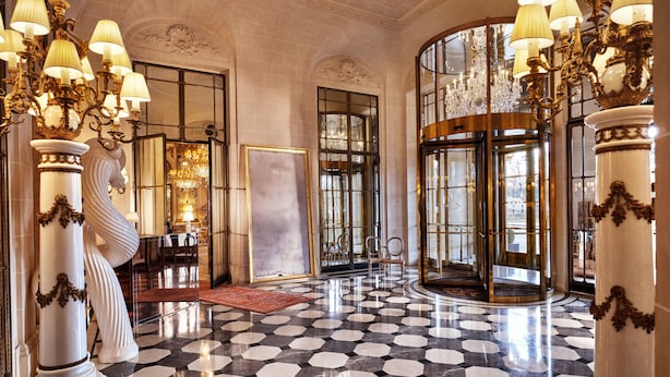 A grand lobby with a black and white checkered floor, ornate columns, and a large chandelier. - Le Meurice - Dorchester Collection (Paris)