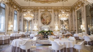 A grand dining room with ornate chandeliers, a central floral arrangement, and classical artwork on the walls. - Le Meurice - Dorchester Collection (Paris)