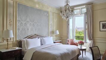 Ein Hotelzimmer mit einem großen Bett, zwei Nachttischen mit Lampen, einer Deckenleuchte und einem Fenster mit Vorhängen, durch das man Grünflächen sieht.