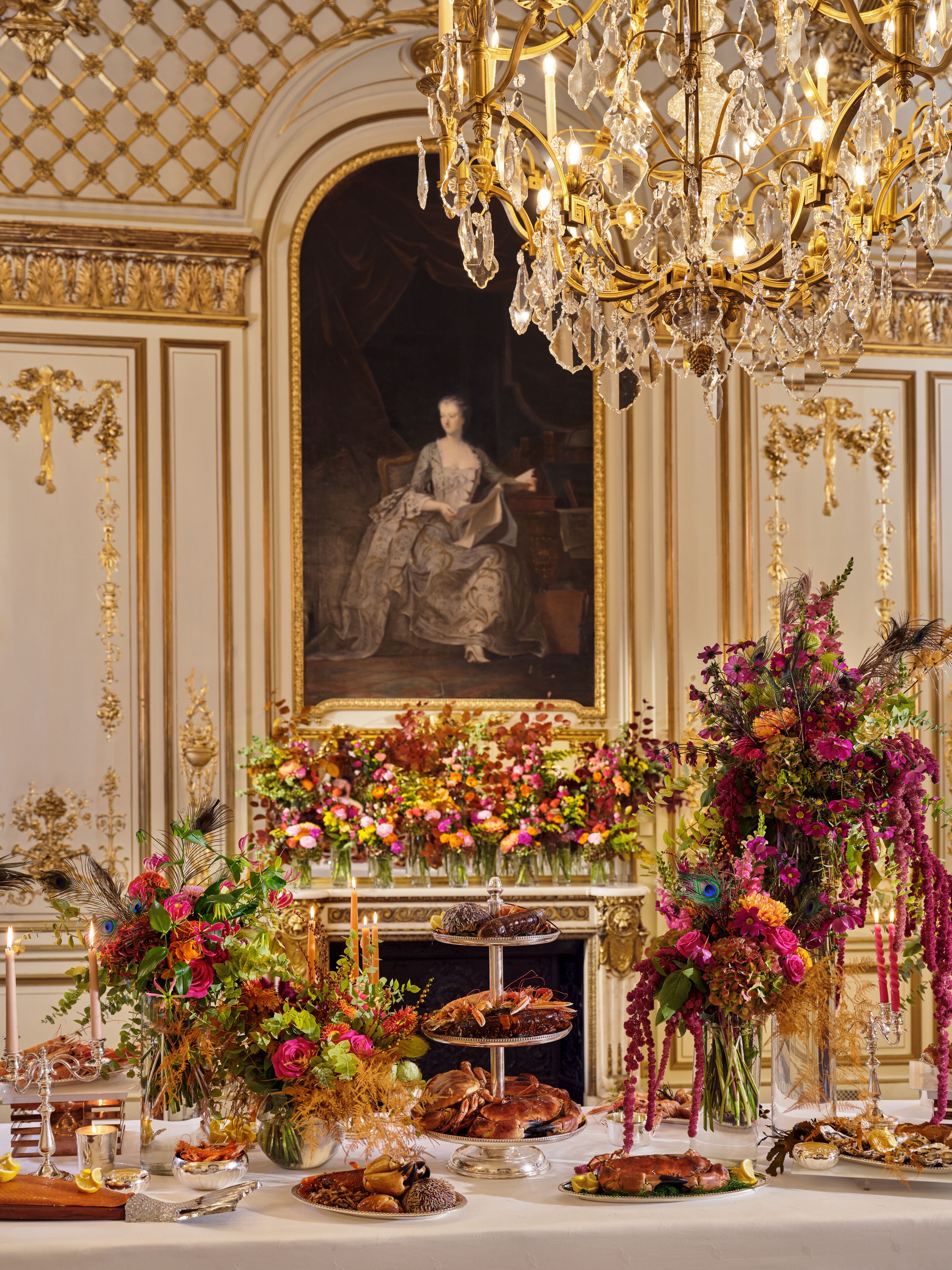 Una habitación opulenta con una gran araña, un retrato de gran tamaño y elaboradas composiciones florales.