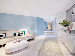 A modern hotel lobby with a curved white sofa, a glass coffee table, and a decorative vase with flowers.