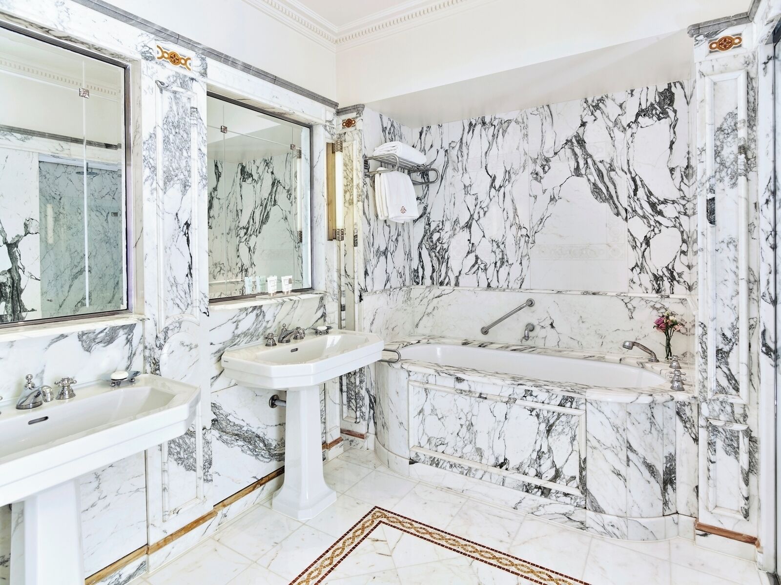 A bathroom with marble walls, a bathtub, and two sinks.