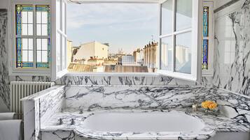 A bathroom with a large marble bathtub, a view of the cityscape through large windows, and a radiator.
